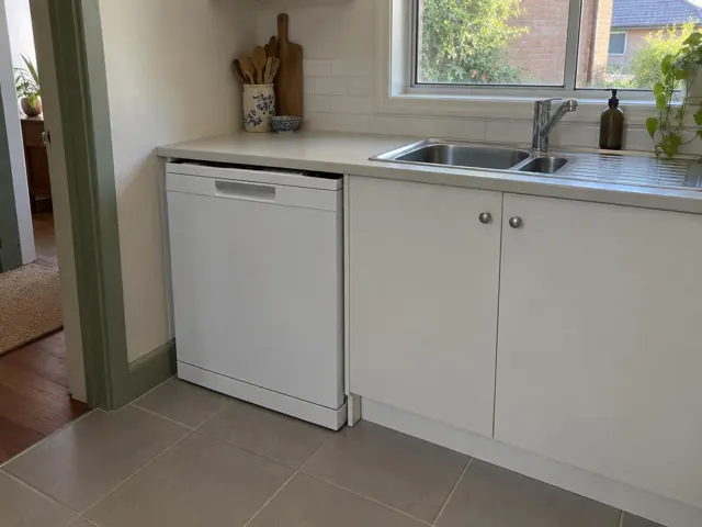 Kitchen with a white dishwasher under a benchtop beside a stainless sink and tiled splashback in Mayfield
