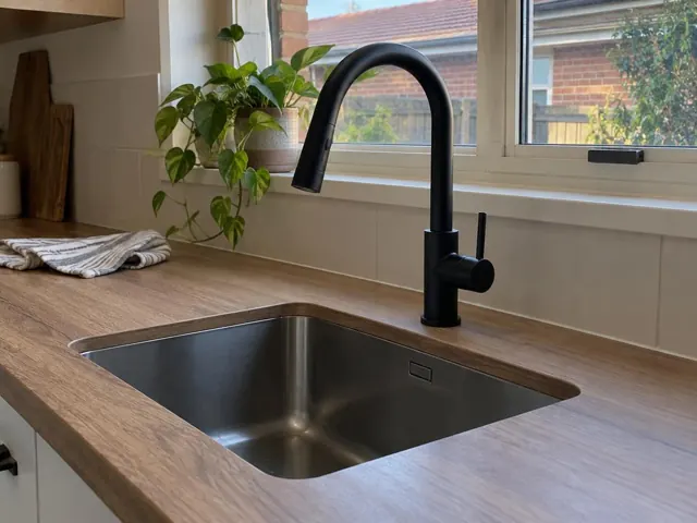 Black gooseneck kitchen mixer above a stainless sink in a modern timber kitchen in Mayfield North
