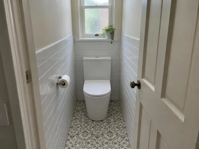 White toilet in a narrow tiled bathroom with patterned floor and window in Islington